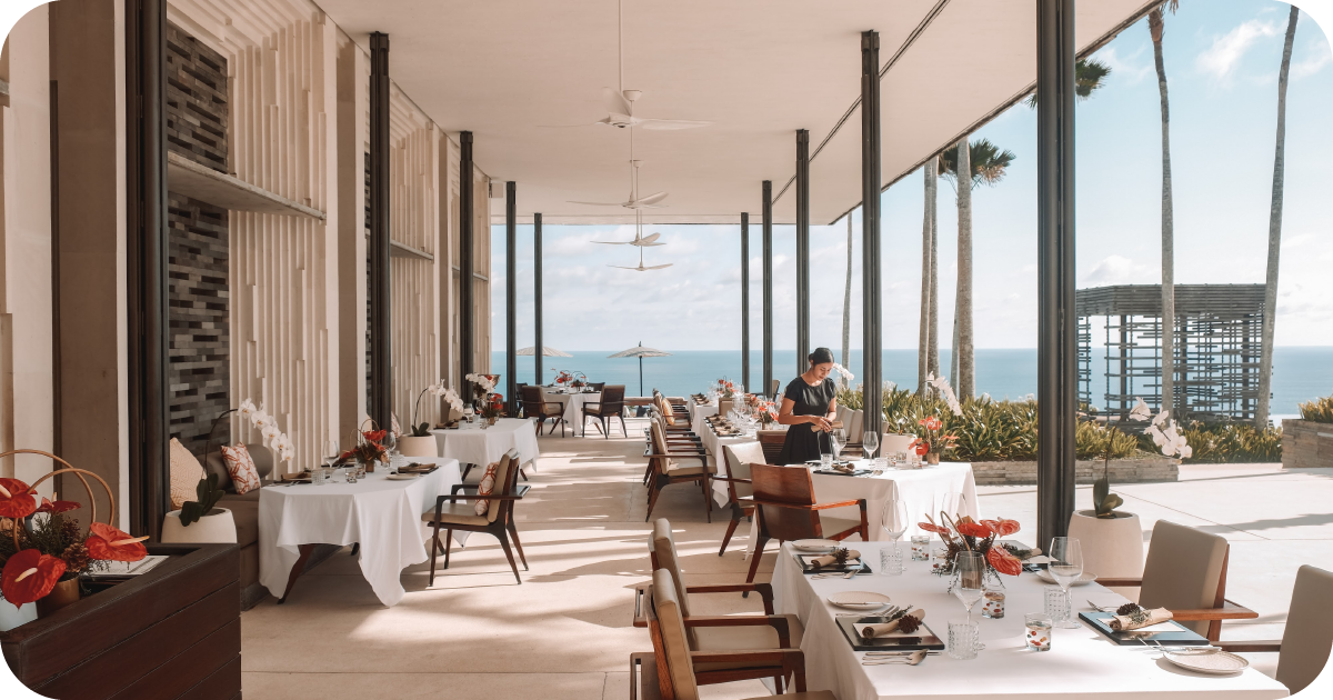 Open-air oceanview dining room with white tablecloths and ceiling fans