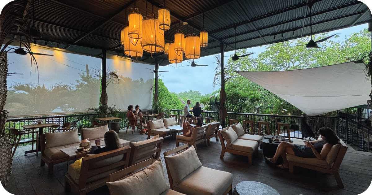 Open-air terrace lounge with lantern pendants, cushioned sofas, garden view