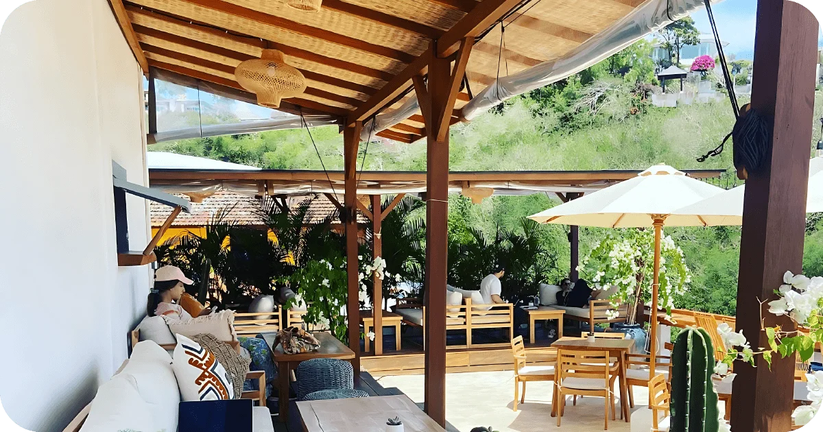 Open-air terrace with wooden sofas, white umbrellas, and tropical plants
