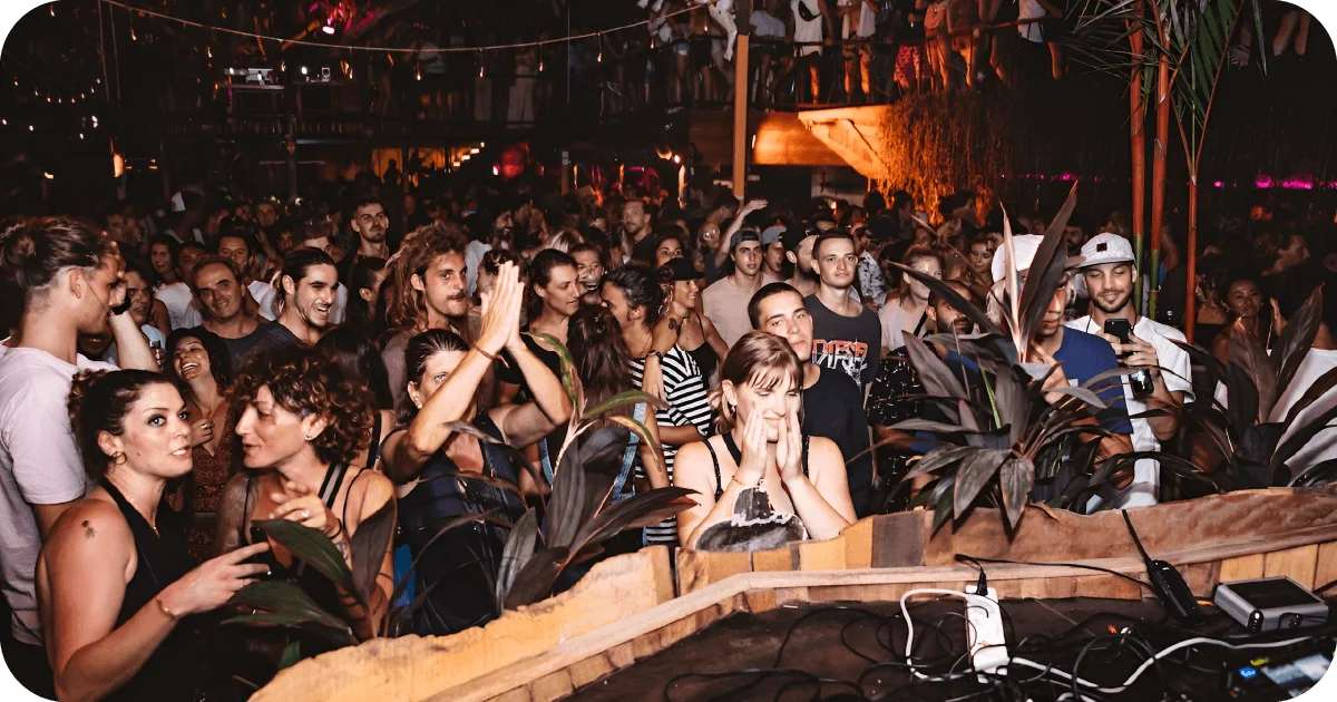 Packed crowd dancing by DJ booth at nighttime event