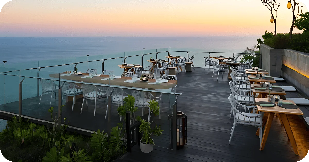 Sunset rooftop deck with glass railing, white chairs, ocean panorama