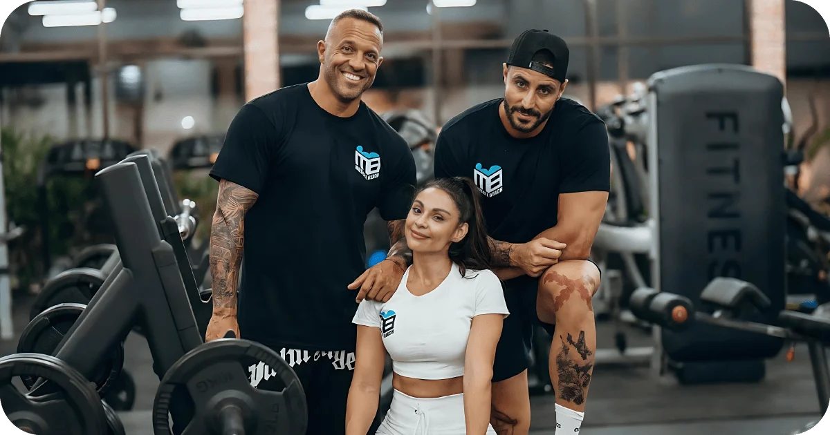 Team in Muscle Beach apparel posing among weight machines