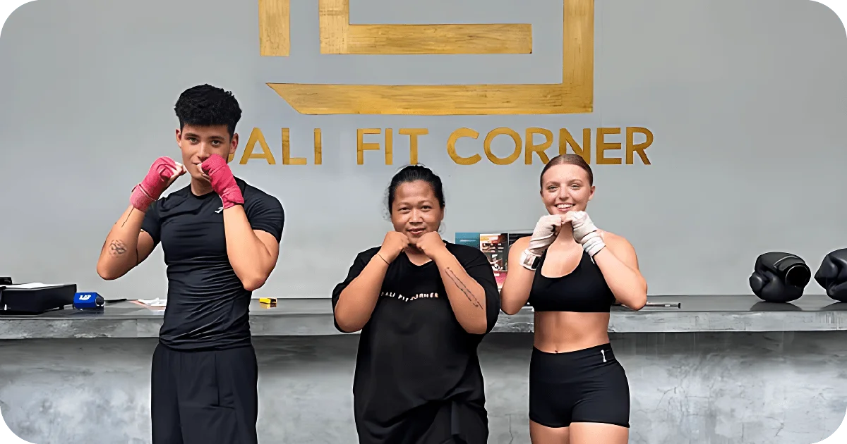 Trio posing with gloves before Bali Fit Corner logo wall