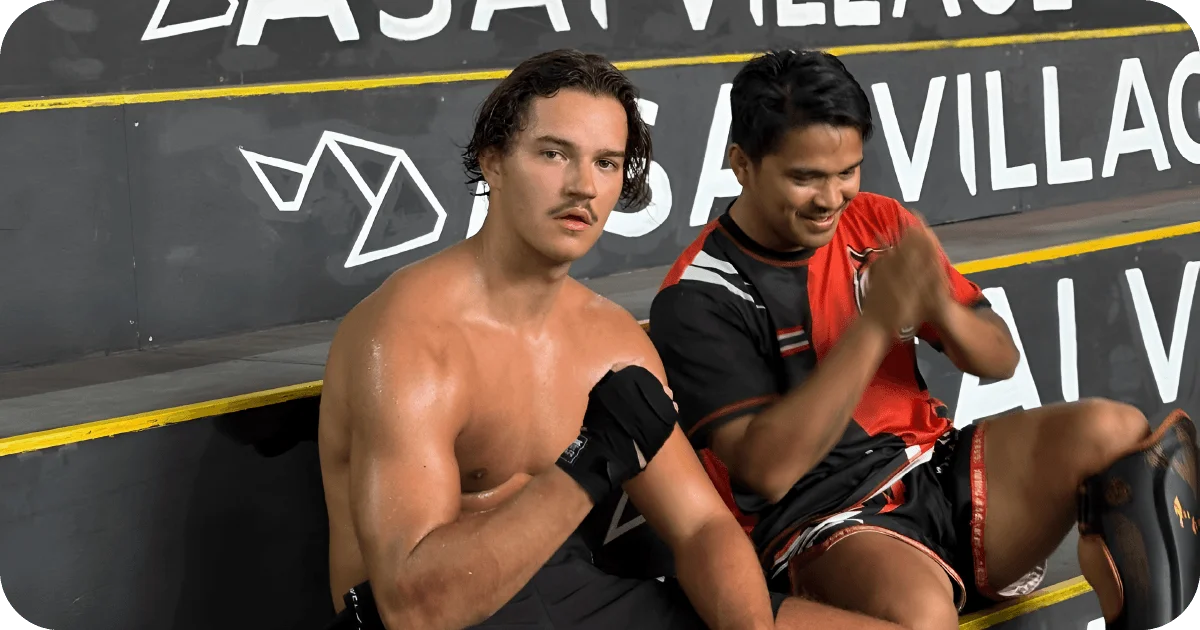 Two Muay Thai athletes resting on steps, hand wraps and shin guards
