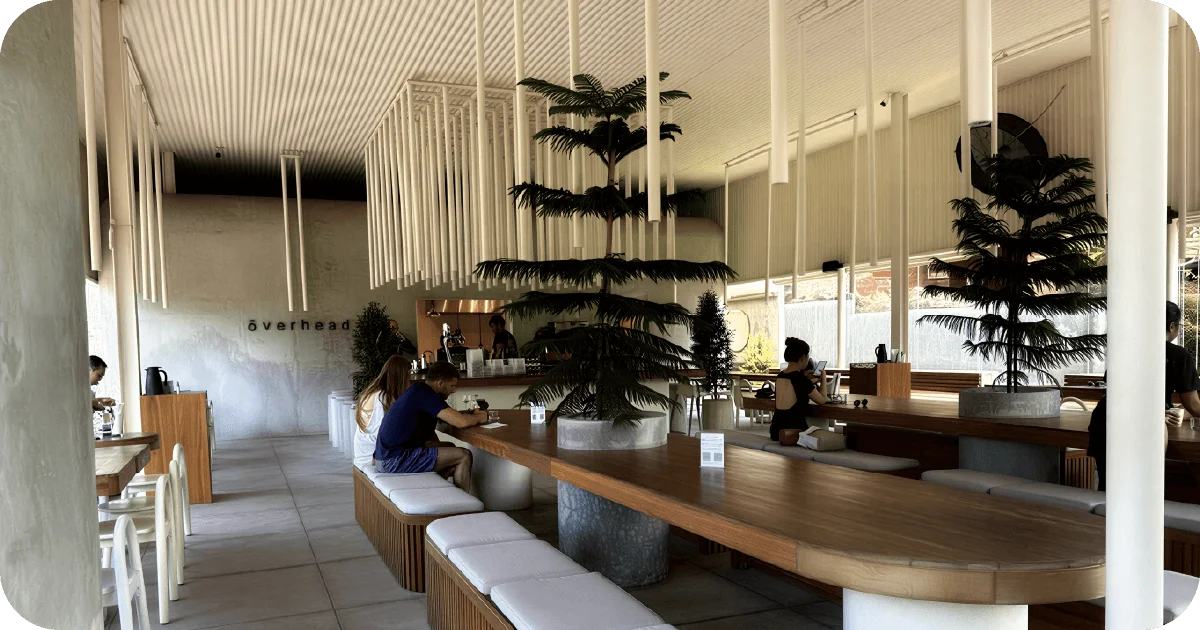 ōverhead interior with long communal table, hanging tube lights, potted trees