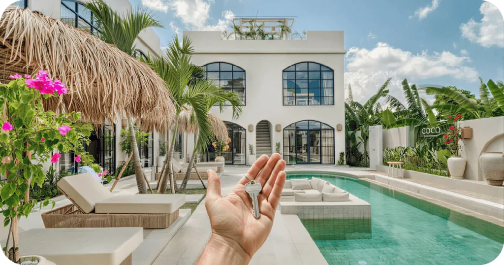 how to buy property in bali: Hand holding keys before modern villa with pool and cabanas